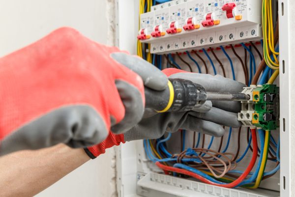 Close up of electrician's hands in working gloves installing and maintainin electrical junction box. Electrical services concept